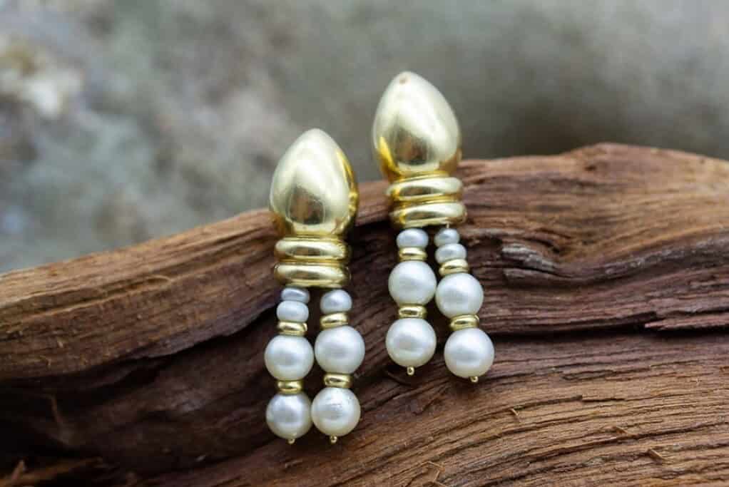 Pendientes de oro con perlas blancas de cultivo sobre madera natural.