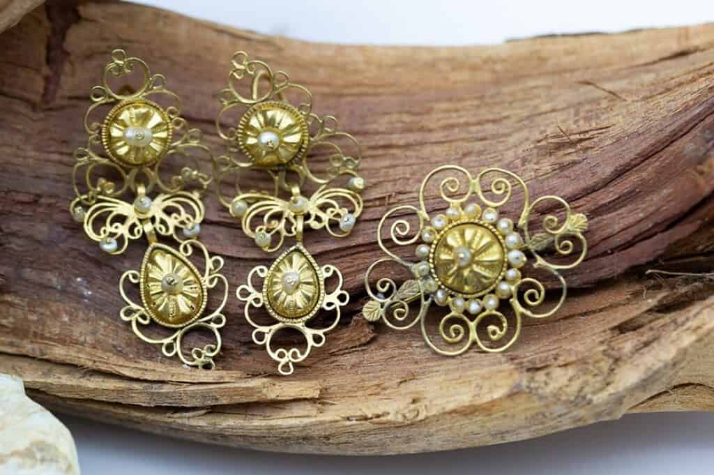 Pendientes y broche de oro con perlas de cultivo, de diseño clásico. Se apoyan en madera natural.