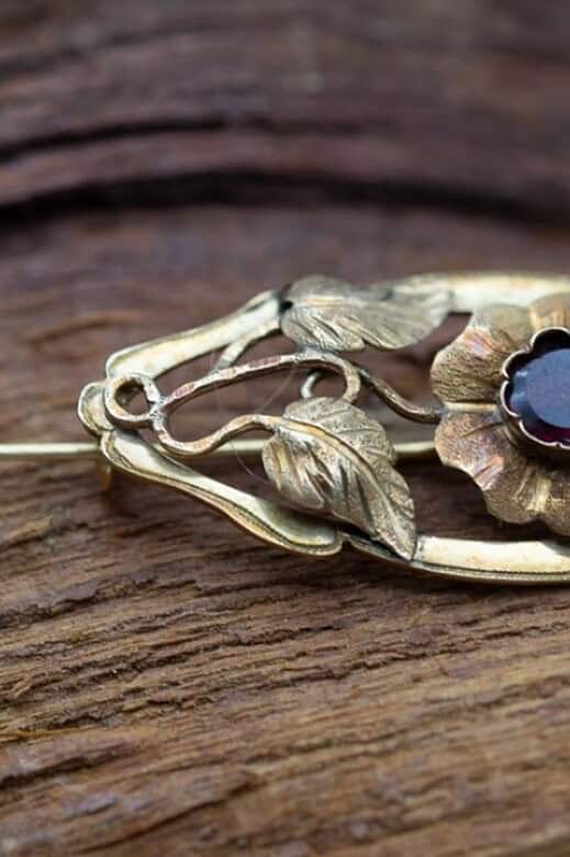 Broche de oro con motivo floral y una gema.
