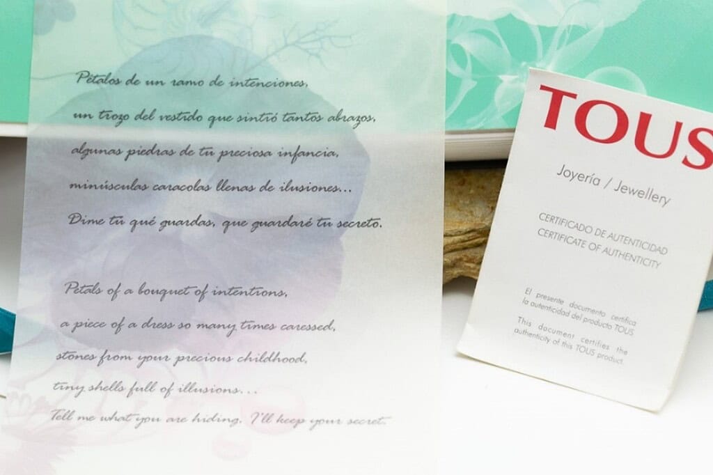 Tarjeta de autenticidad de TOUS joyería y tarjeta con poesía de letras en fondo pastel.